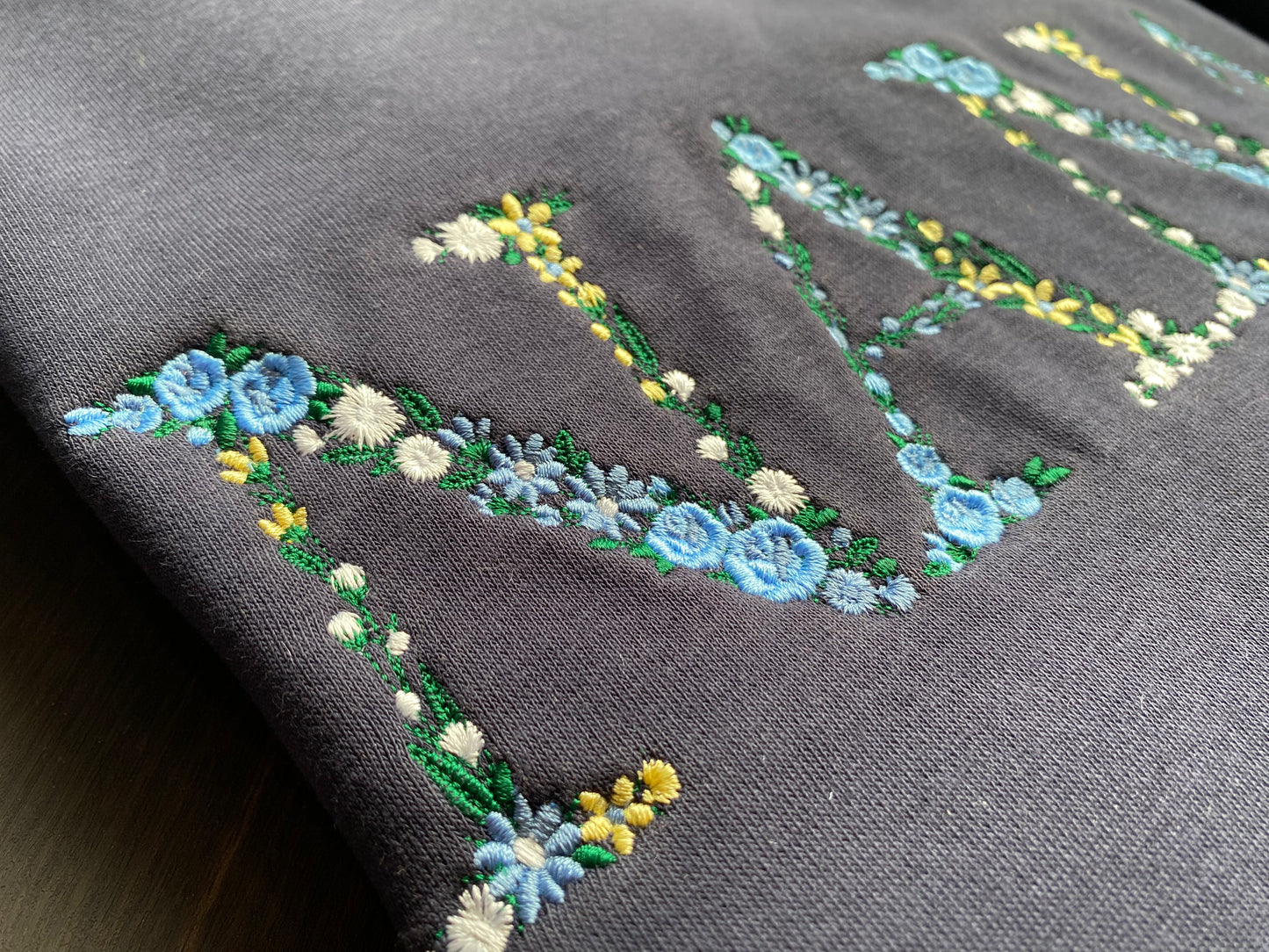 Mẫu thêu áo sweater chữ hoa NANA trên áo nỉ xanh navy, món quà ý nghĩa dành cho người phụ nữ tuyệt vời nhất